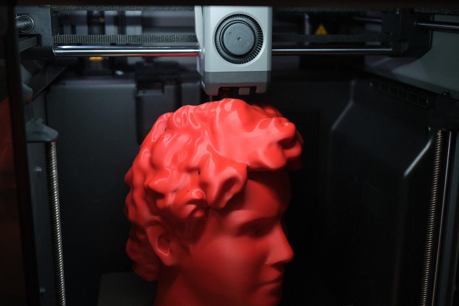 A bust printing in red PLA, the toolhead paused above it
